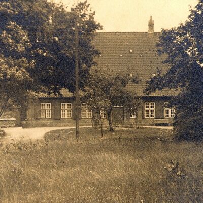 Das Bild zeigt das Pastorat im Jahre 1940 im Eingangsbereich. In der Zeit war Wilhelm Sievers von 1925 bis 1946 Pastor in Schönkirchen (Schautafel auf dem Kirchfriedhof). Nach ihm wurde das heute rechts neben dem Weg zum Pastorat stehende Kirchenbüro und Gemeindehaus benannt.